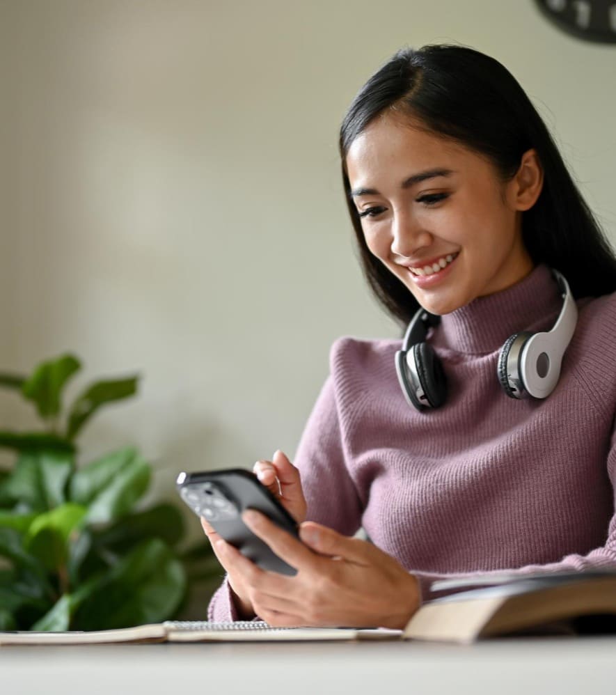 Smiling woman with headphones around her neck using a smartphone at her desk